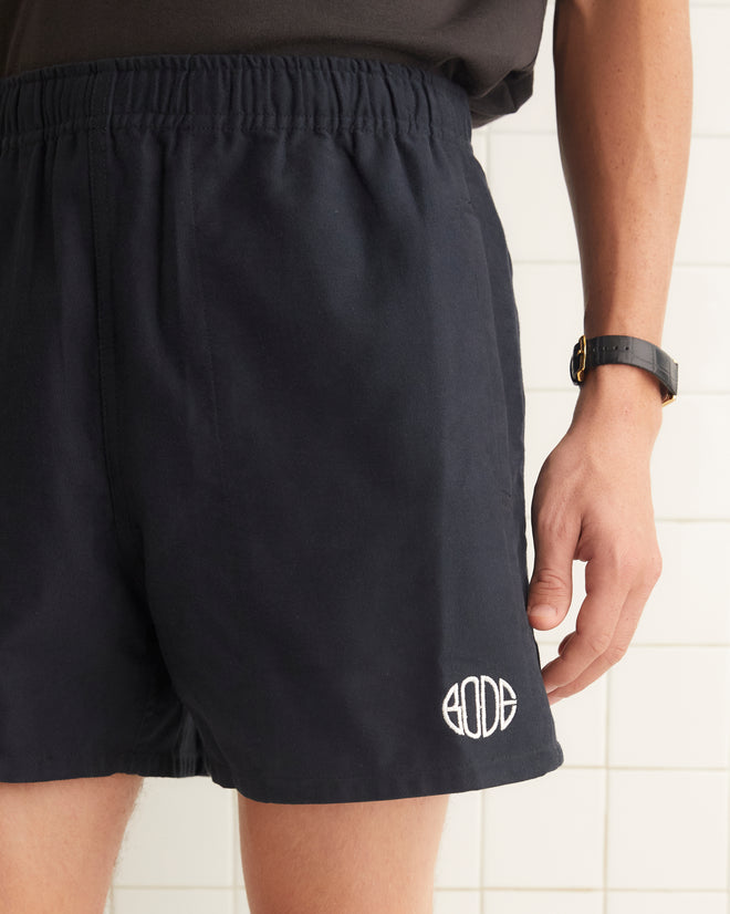 Navy cotton rugby shorts with short inseam and wide leg opening. The shorts are embroidered with a Bode logo.