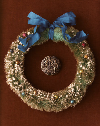 Centered around a circular relief decoration featuring a bronze motif, the Christmas wreath includes a blue bow and colorful ornaments.