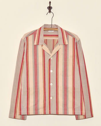 A Fire Blanket Long Sleeve Shirt (Size M) with red, beige, and gray vertical stripes hangs on a hook against a plain wall—crafted in New York.