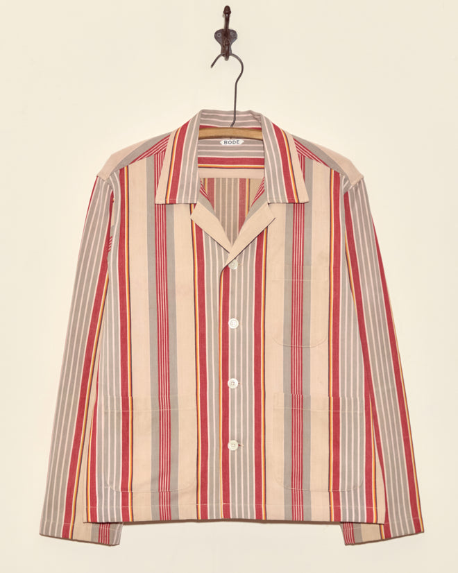A Fire Blanket Long Sleeve Shirt (Size M) with red, beige, and gray vertical stripes hangs on a hook against a plain wall—crafted in New York.