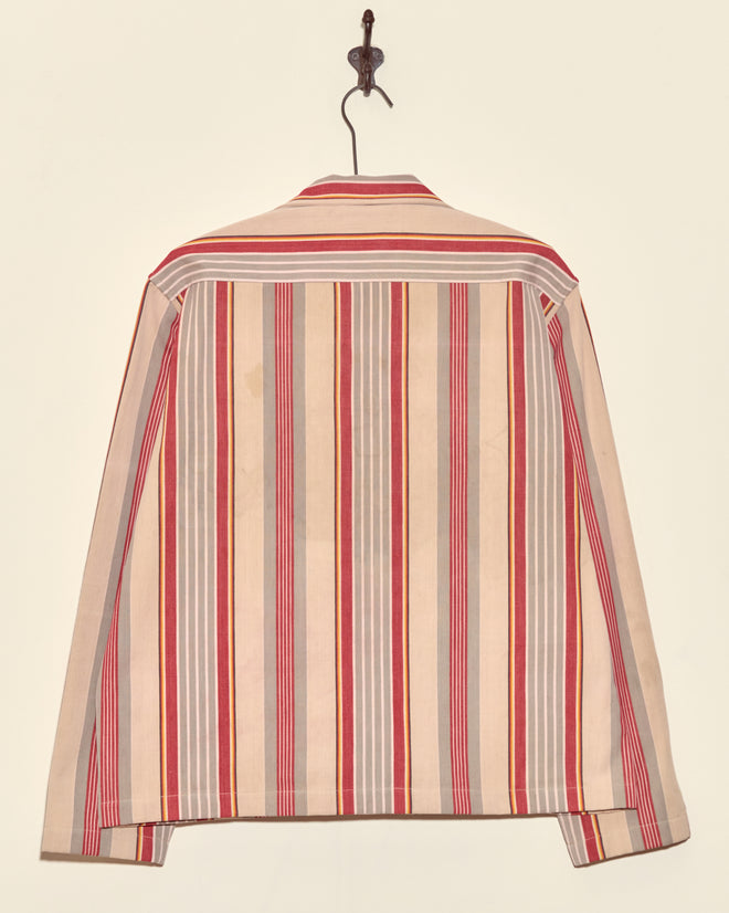 A unique Fire Blanket Long Sleeve Shirt (size M) with red, beige, and gray vertical stripes hangs on a hook against a light wall—a modern take on antique ticking style.