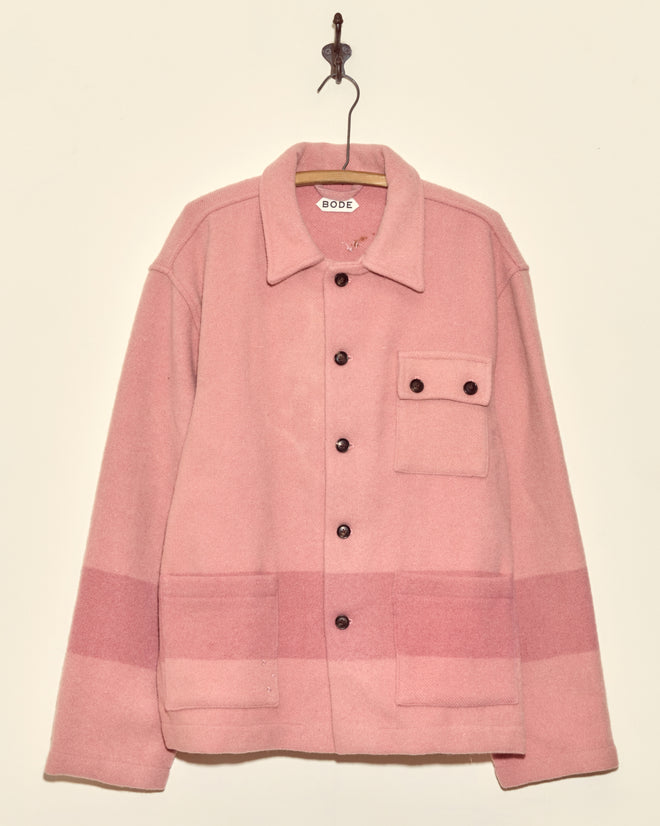 The Flamingo Pink Line Jacket (XL/XXL), a unique midcentury wool piece with black buttons and front pockets, hangs from a simple hook on a beige wall.