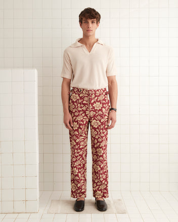 A pair of Floral Corduroy Trousers, featuring a high-rise straight-leg design and crafted from 1960s deadstock upholstery fabric, hangs on a wooden hanger against a plain wall.