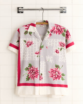 Floral Kale Shirt - XS/S: A unique short-sleeve button-up with pink floral patterns and red accents, inspired by 1950s-1960s style, displayed on a tile wall.