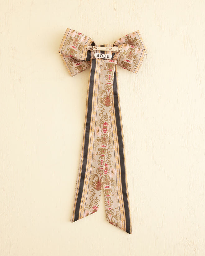 The Floret Brocade Bow Barrette, featuring intricate patterns and long ribbon tails crafted from exquisite brocade fabric, stands out elegantly against a light background.