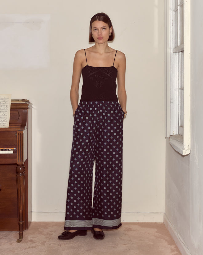 A woman wearing black with Foyer Diamond Pants stands indoors near a piano and window.