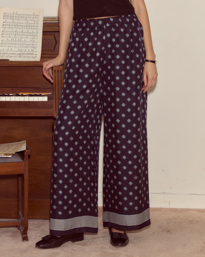 A person wearing Foyer Diamond Pants stands by a piano with sheet music on it.