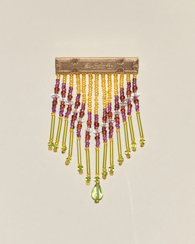 Fringe Barrette featuring a rectangular brass plate pin adorned with dangling yellow, green, and red beads, finished with a green teardrop bead centerpiece.