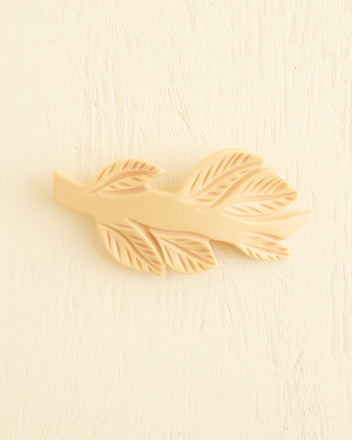 The Frond Barrette is a cream-colored, leaf-shaped accessory featuring intricate textured leaf details on a light background, capturing the nostalgic charm of Bakelite in a soft butterscotch shade.