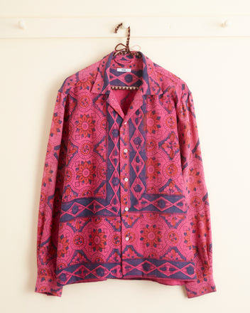 A Fuchsia Print Long Sleeve Shirt in size M/L, adorned with an intricate pink and blue geometric pattern, hangs on a wall hook.