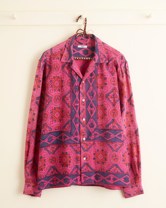 A Fuchsia Print Long Sleeve Shirt in size M/L, adorned with an intricate pink and blue geometric pattern, hangs on a wall hook.