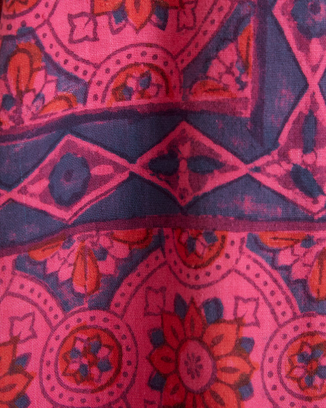 A Fuchsia Print Long Sleeve Shirt in size M/L, adorned with an intricate pink and blue geometric pattern, hangs on a wall hook.