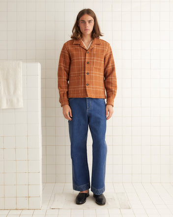 Person with long hair wearing a Centennial Plaid Long Sleeve Shirt and blue jeans standing in a white-tiled room, evoking a hint of 1960s design.