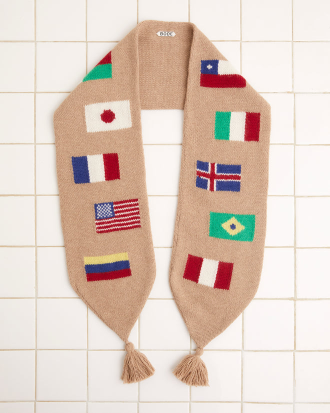 Round-the-World Scarf - Tan with an intarsia flag pattern displaying international flags such as Japan, Italy, France, USA, and Brazil on a tiled background. Made from soft merino wool for warmth and style.