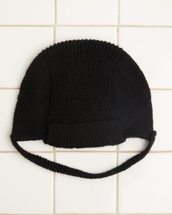 The Terrain Hat in black, crafted from merino wool and featuring a chin strap, is elegantly displayed on a white tiled surface.