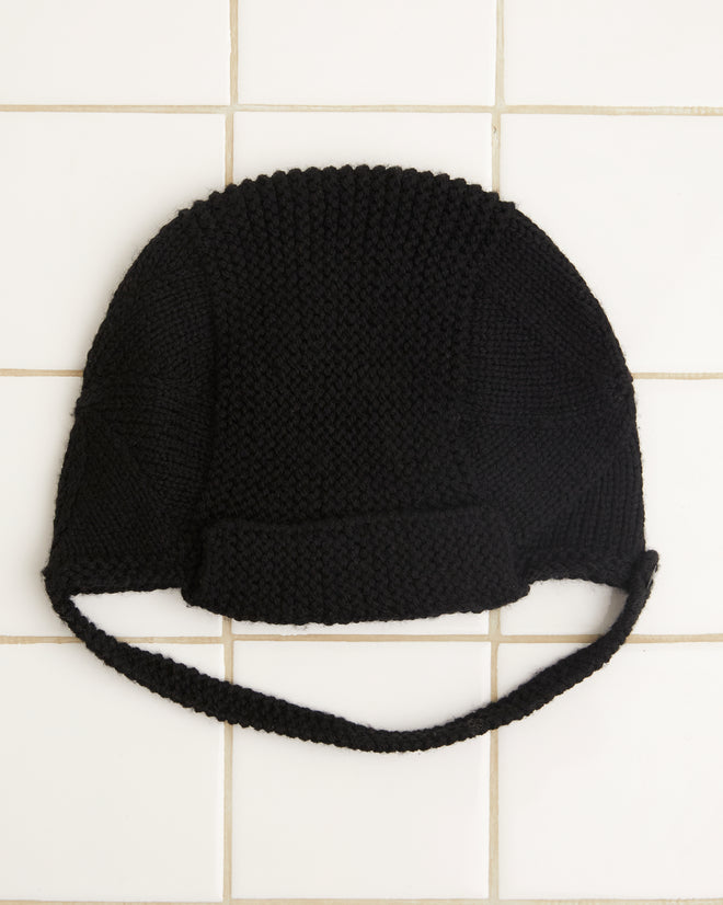 The Terrain Hat - Black, a Merino wool knit cap featuring a chin strap, is elegantly displayed on a white tiled surface, making it the perfect addition to your collection of stylish accessories.