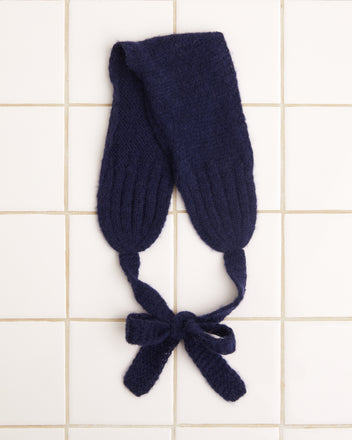 A navy blue knitted headband, inspired by 1940s-1960s reproduction styles and crafted from an alpaca/merino blend, gracefully tied in a bow on a white tiled surface.