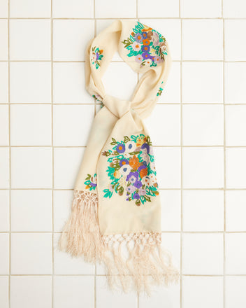 Flower Language Scarf in beige, featuring vibrant floral embroidery and fringed ends, showcased against a tile background.