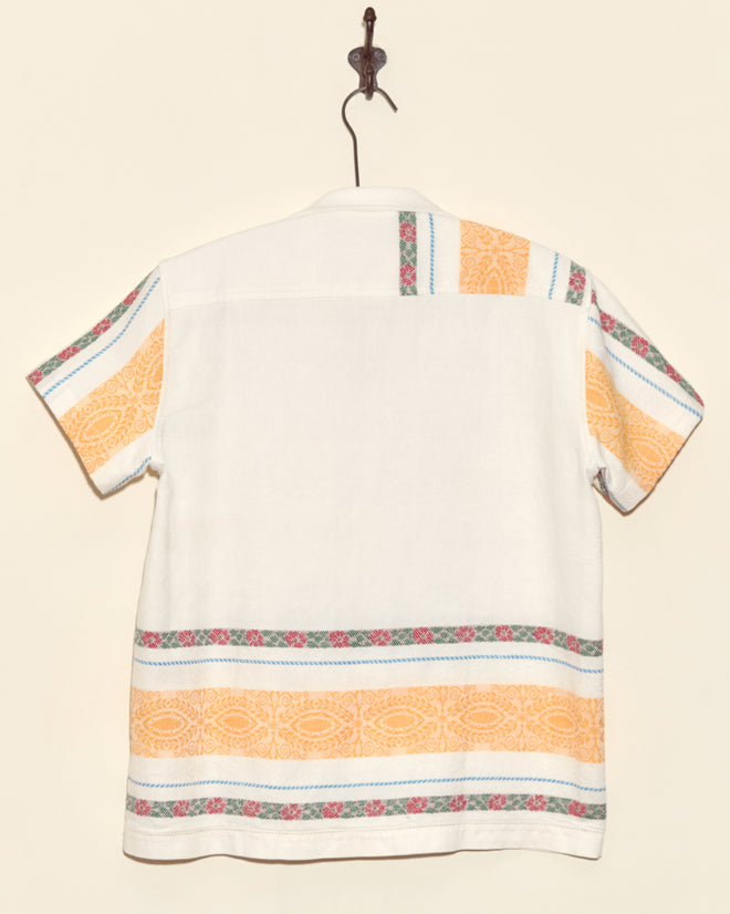 The Geography Stripe Short Sleeve Shirt - XS features a white base with orange and multicolored stripes, crafted by hand from a vintage tablecloth and shown hanging on a hook.