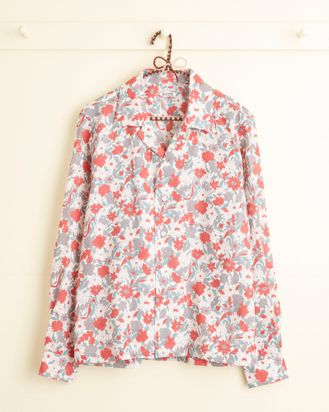 A Gerbera Grove Long Sleeve Shirt - S, adorned with a pink and red floral pattern, hangs on a wall hook, showcasing its timeless charm.