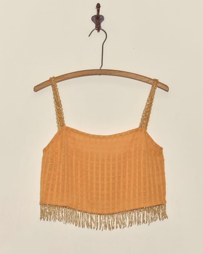 Gilt Rosetta Tank - S: An orange crop top with vintage beaded trim and fringe hem, displayed on a wooden hanger against a plain wall—a unique statement piece for your wardrobe.