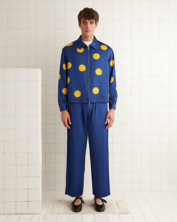 A person in a striking Gold Medal Jacket, featuring a blue outfit with yellow polka dots, stands gracefully in a tiled room.