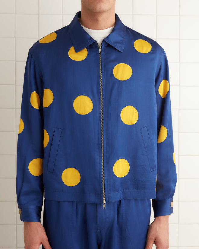 A person in a striking Gold Medal Jacket, featuring a blue outfit with yellow polka dots, stands gracefully in a tiled room.