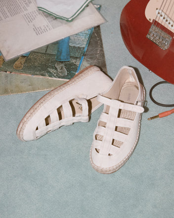 Peggy Espadrilles - Natural, featuring a white woven design and jute sole, rest on a blue carpet beside a red electric guitar and vinyl records—perfect summer shoes for music lovers.