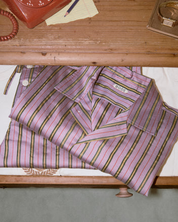 A folded Alumni Stripe Long Sleeve Shirt - Purple rests on a wooden desk beside a red rotary phone and papers, capturing a vintage vibe inspired by the 1960s-1980s.