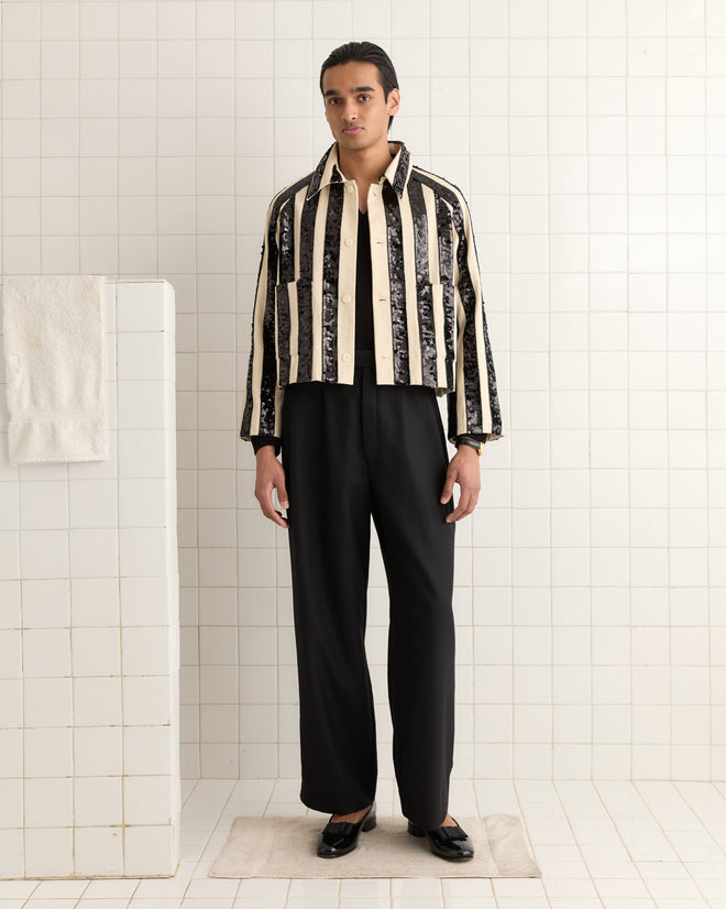 A person wearing the Grandstand Cropped Jacket with black and white sequin stripes and black pants stands in a tiled room, showcasing a classic boxy workwear look with a neutral expression.