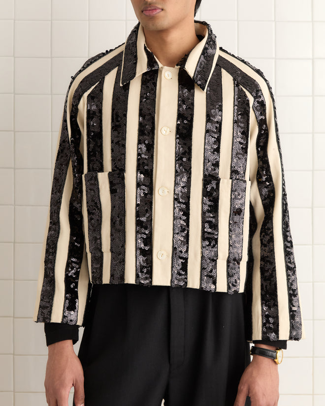 Someone wearing the Grandstand Cropped Jacket, featuring a black and white striped sequin design in a boxy fit, stands against a tiled background.