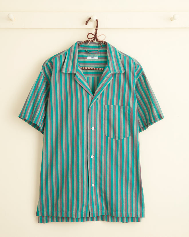 A unique Grassy Stripe Shirt - XXL, featuring short sleeves, a button-up design, and vertical stripes in shades of blue, teal, red, and gray hangs on a white wall hook.