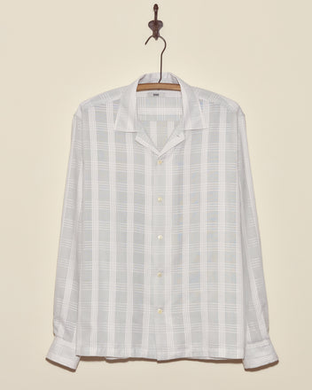 The Grayscale Long Sleeve Shirt - L/XL, made from deadstock plaid shirting fabric, hangs on a wooden hanger against a beige wall.