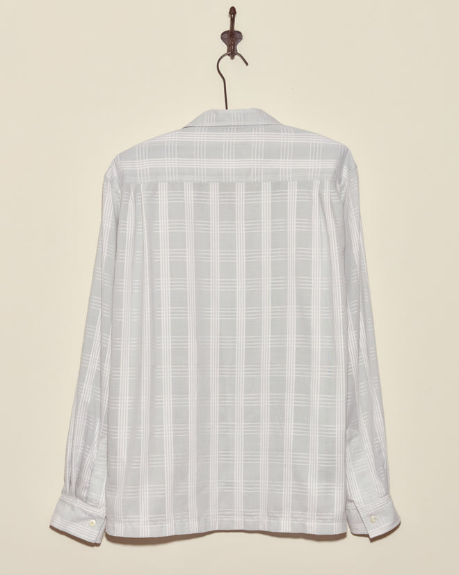 The Grayscale Long Sleeve Shirt - L/XL, crafted from deadstock plaid shirting fabric in light gray, hangs on a hook against a cream wall.