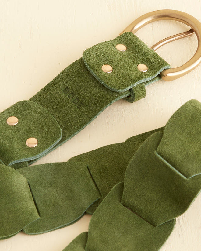 The Suede Link Belt - Green, inspired by '70s fashion, features a woven design crafted from 100% green suede and is adorned with a brass buckle. It is showcased on a light surface.