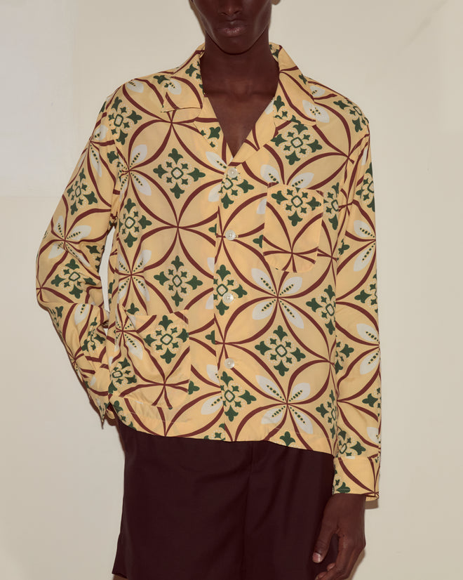 A person wears the Greer Long Sleeve Shirt in yellow geometric pattern with brown shorts, standing against a plain light background.