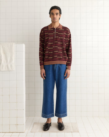 Wearing the Gridiron Quarter-Zip and blue jeans, a person stands on a white bathroom mat against a tiled wall.