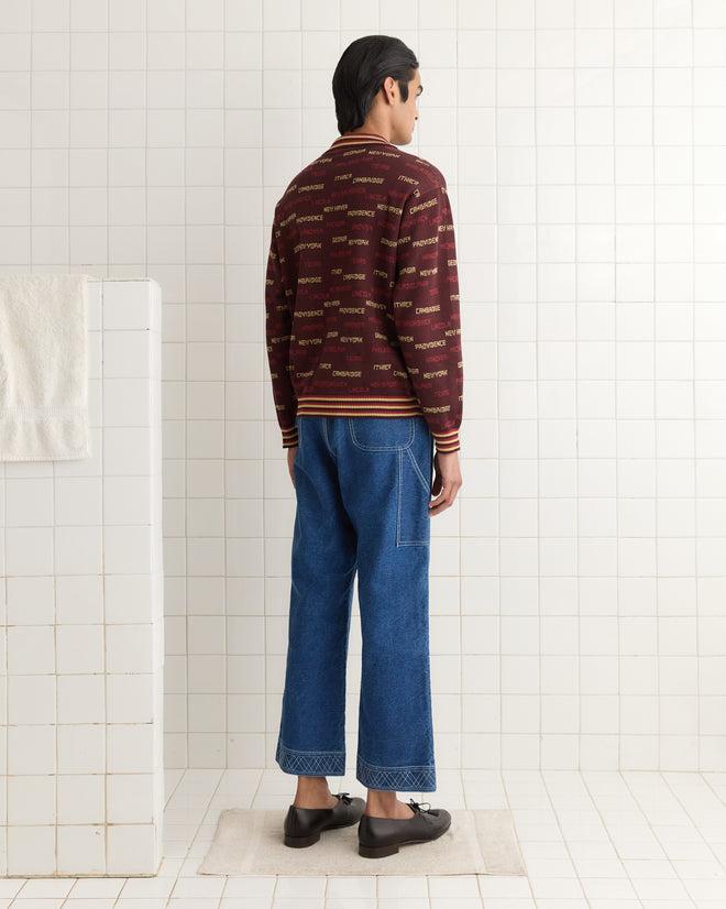 A person in a Gridiron Quarter-Zip and blue jeans stands in a tiled room, facing away from the camera.