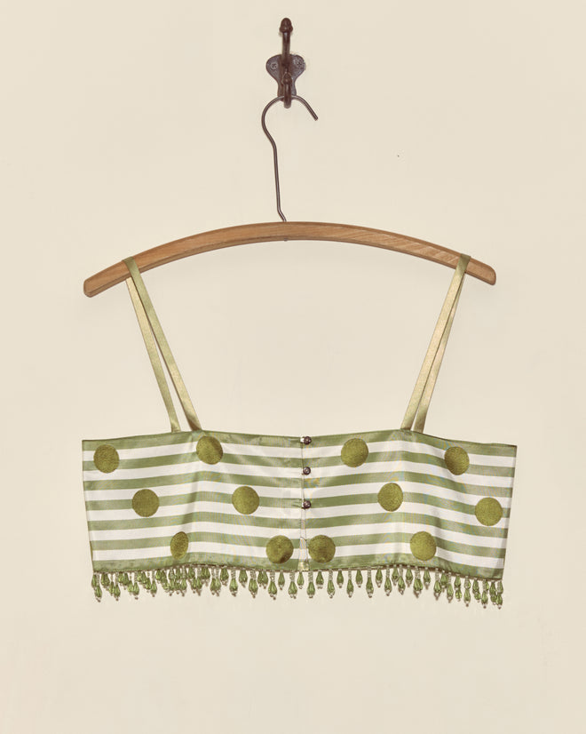 The Green Note Bra - S features green and white stripes, polka dots, beaded fringe, and a Staron jacquard ribbon accent, displayed elegantly on a wooden hanger against a pale wall.
