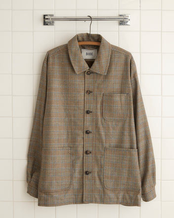 The Helmsley Franck Jacket - XL/XXL, made from unique 1960s suiting fabric and featuring a collar and buttons, hangs on a metal rack against a tiled wall, highlighting its distinctive charm.