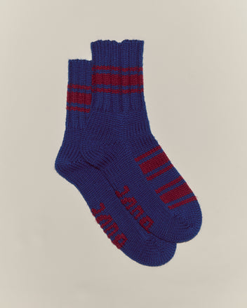 The Herrington Stripe Socks - Blue are chunky knit merino wool socks featuring red stripes and red text on the soles, shown on a plain background.