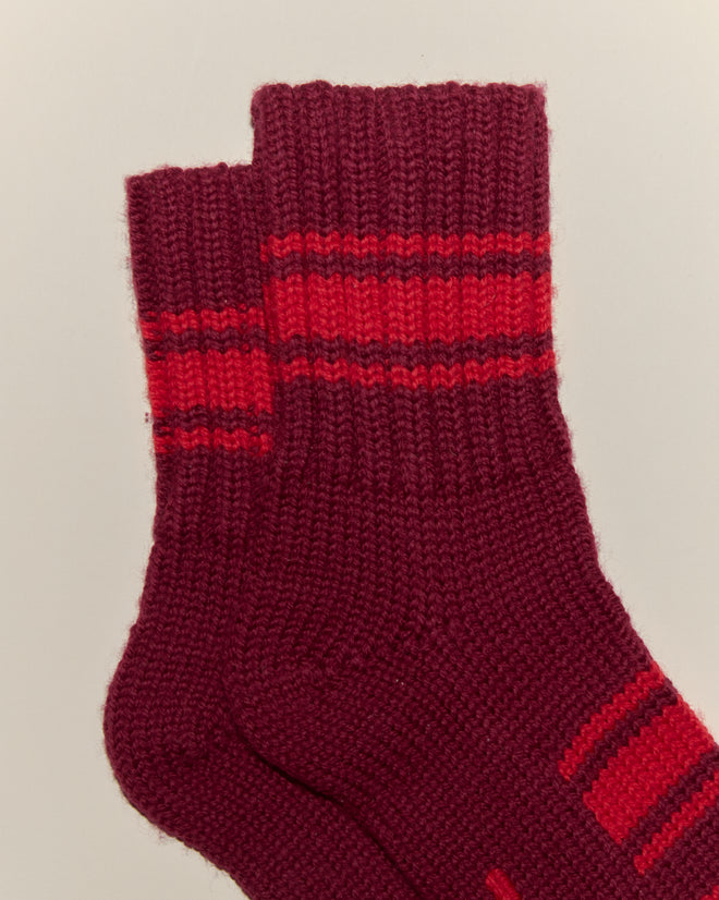 The Herrington Stripe Socks - Burgundy are maroon merino wool knit socks featuring two red stripes near the top, shown laid flat on a light background.