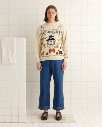 Someone wearing the Homestead Sampler Sweater and jeans is standing in a tiled room with a towel on the wall, highlighting classic New England knitwear.