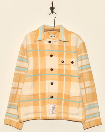 The Horizon Plaid Blanket Jacket - XS/S is a unique yellow plaid wool jacket with turquoise and white stripes, black buttons, and large front pockets, made in New York. It's pictured hanging on a hook.