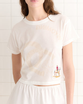 Person wearing a sheer cotton Horseshoes Tee featuring a subtle design and small illustration of a horse rider, evoking vintage tees from past tournaments.