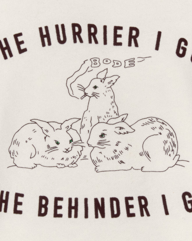 The Hurrier Sweatshirt features three rabbits—one smoking—and the phrase "The hurrier I go, the behinder I get," inspired by Lewis Carroll’s White Rabbit. Finished with black and white striped trim for a unique style.