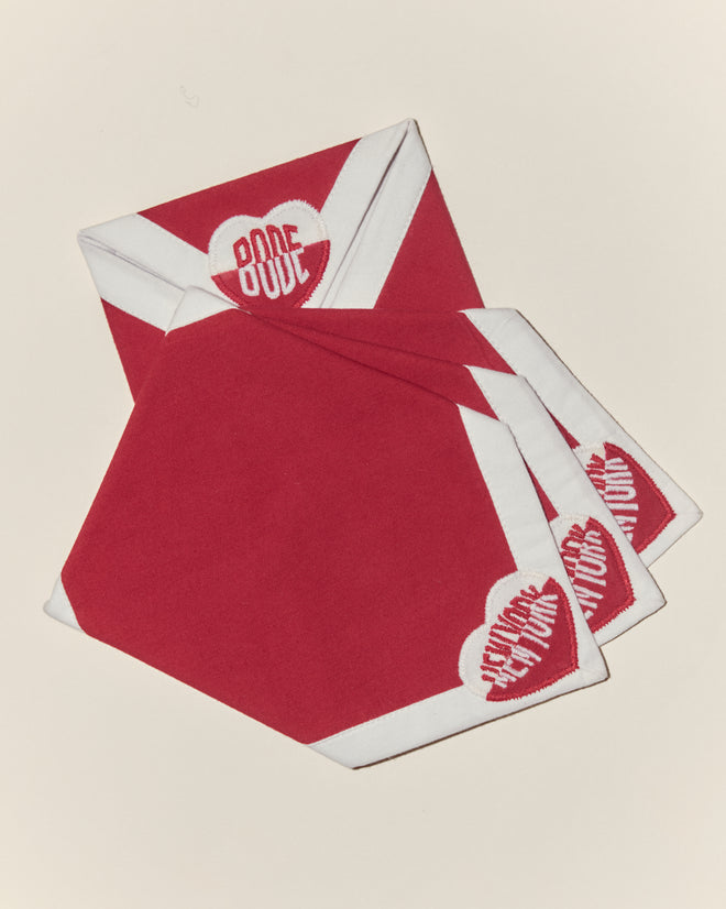 Set of four Heart Deco New York Cocktail Napkins in red and white cotton voile, each with a heart appliqué and “BODE NEW YORK” logo on two corners.