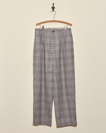 The Ice Sled Wool Trousers - MULTI are gray plaid pants displayed on a wooden hanger against a plain white wall.