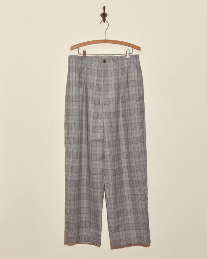The Ice Sled Wool Trousers - MULTI are gray plaid pants displayed on a wooden hanger against a plain white wall.