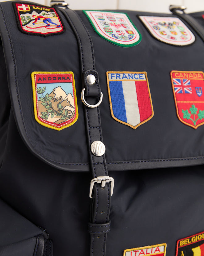 The Interrail Rucksack is a black bag decorated with colorful flag patches of France, Canada, and Switzerland—perfect for travelers seeking a stylish accessory.